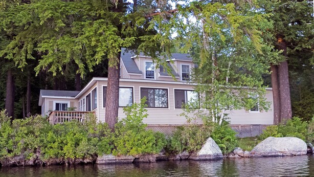 Une maison au bord d’un lac, avec un quai, entourée d’arbres et de rochers.