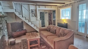 Un salon avec un escalier, un canapé, une télévision et une lampe.