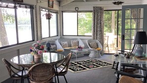Un salon chaleureux avec une table ronde en verre, des fauteuils en osier, un canapé agrémenté de coussins à motifs et un lustre.