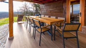 Terraza de madera al aire libre con una mesa larga y sillas, una lámpara colgante y vistas del paisaje.