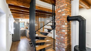 Una escalera de madera con barandillas negras que conduce a una cocina con pared de ladrillo y un tubo negro.