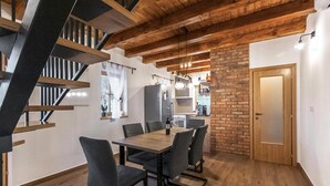 Un comedor con una mesa y sillas de madera, una cocina al fondo y una escalera con vigas de madera.