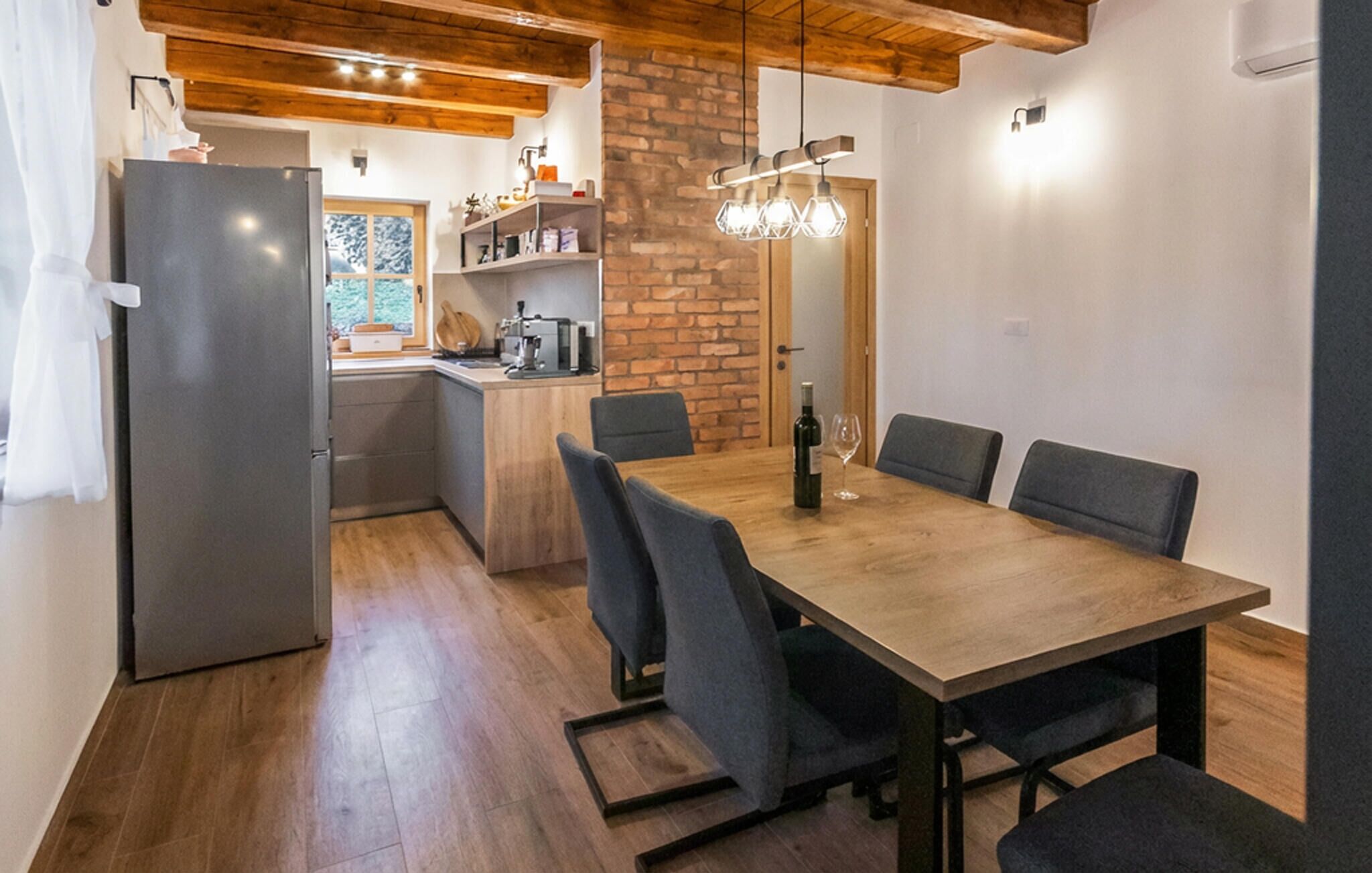 Une cuisine moderne avec une table et des chaises en bois, un réfrigérateur et un mur en briques.