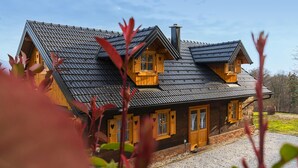 Una casa de madera de dos pisos, con un techo pronunciado, múltiples ventanas con contraventanas y una chimenea.