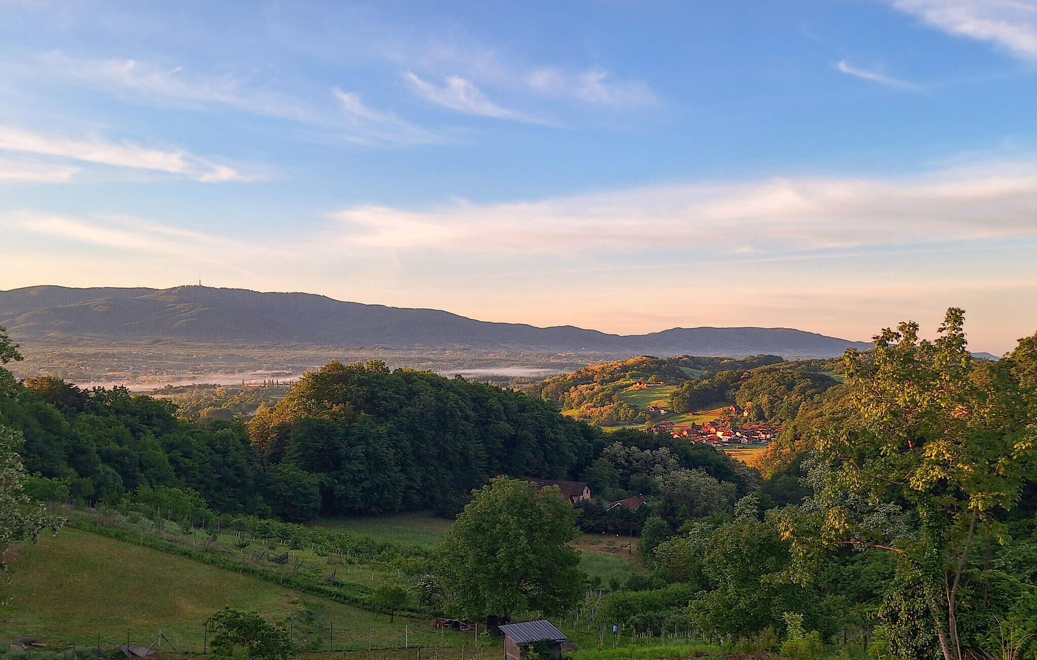 Un paisaje rural con colinas ondulantes, un pequeño pueblo y cielo despejado.