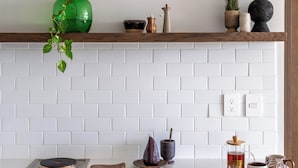 A kitchen with white subway tiles, a wooden countertop, and a shelf with decorative items.