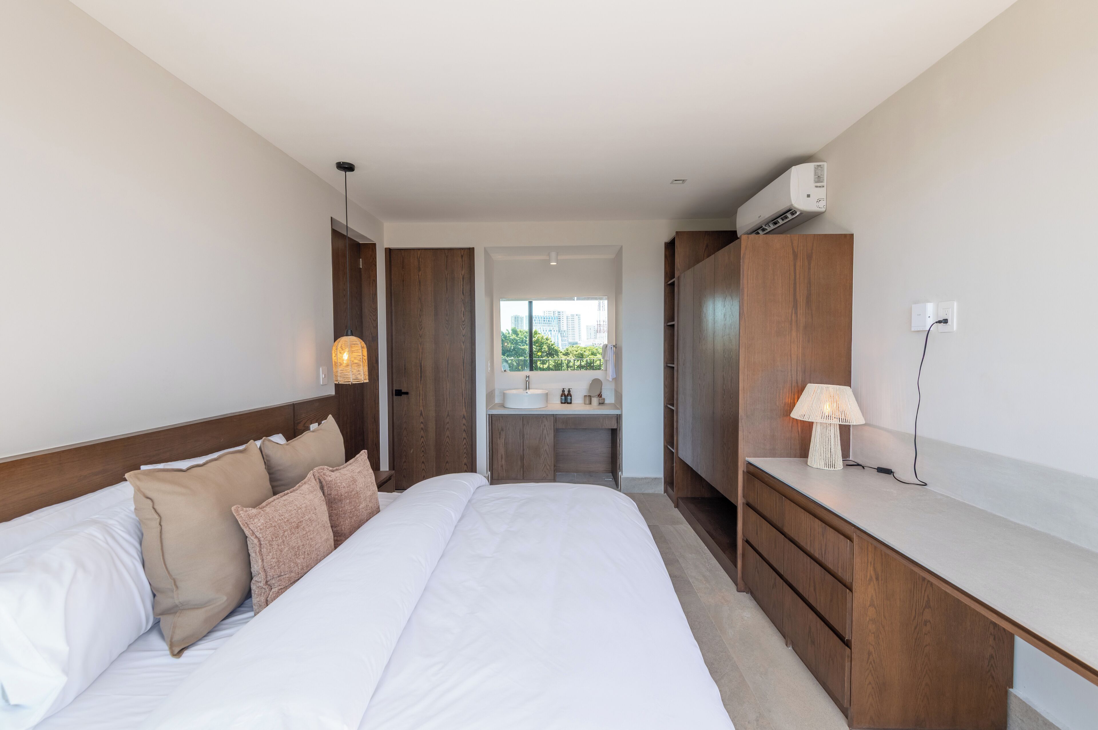 Ein modernes Hotelzimmer mit einem großen Bett, einem Holzschrank und einem Badezimmer mit Waschbecken und Spiegel.