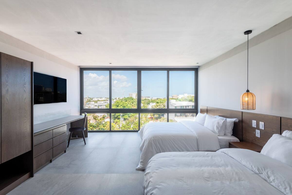 Une chambre d’hôtel moderne dotée d’une grande fenêtre, d’un bureau et de deux lits.