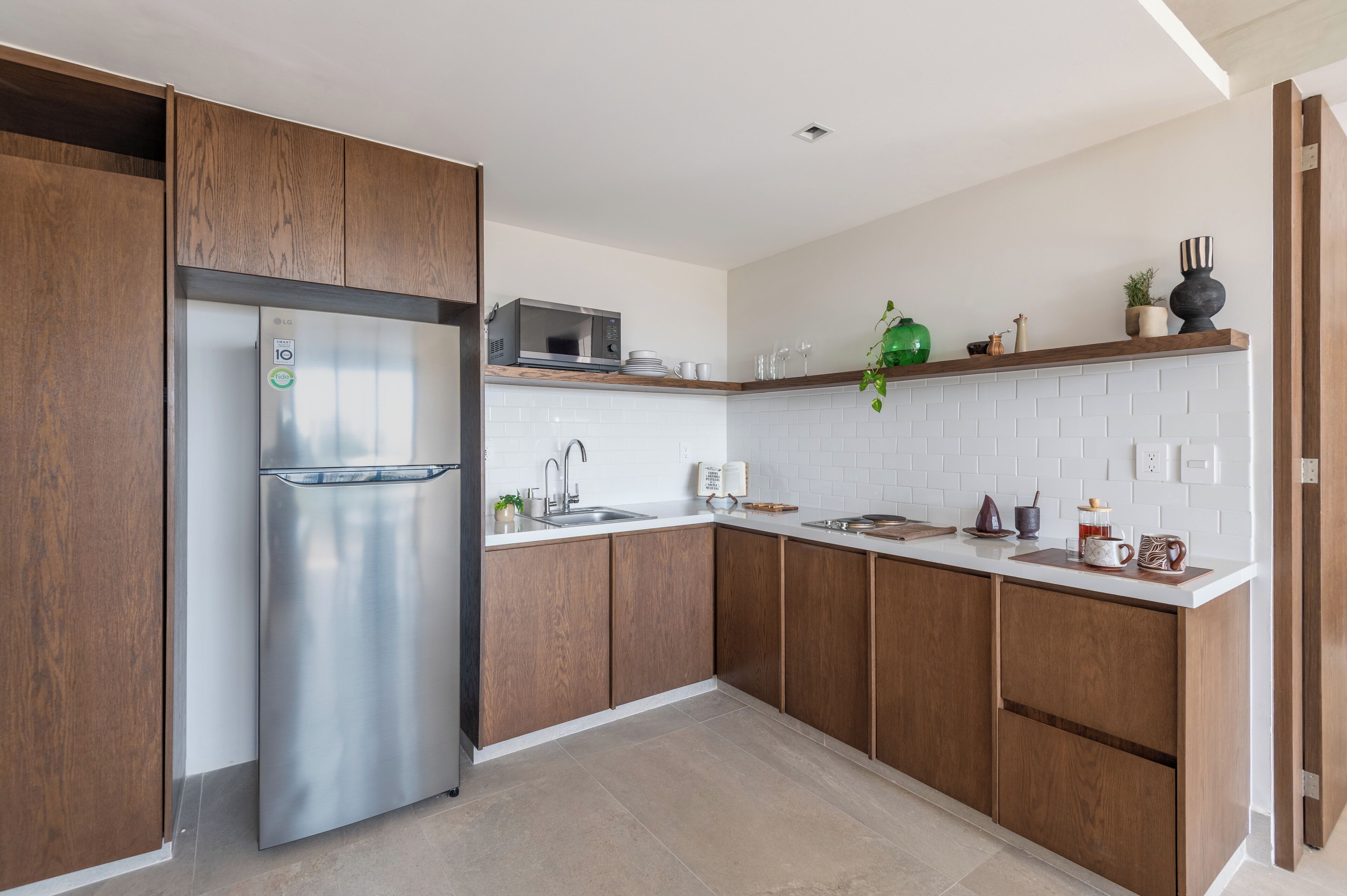 Una cocina moderna con armarios de madera, un refrigerador de acero inoxidable, un microondas y un salpicadero de azulejos blancos.