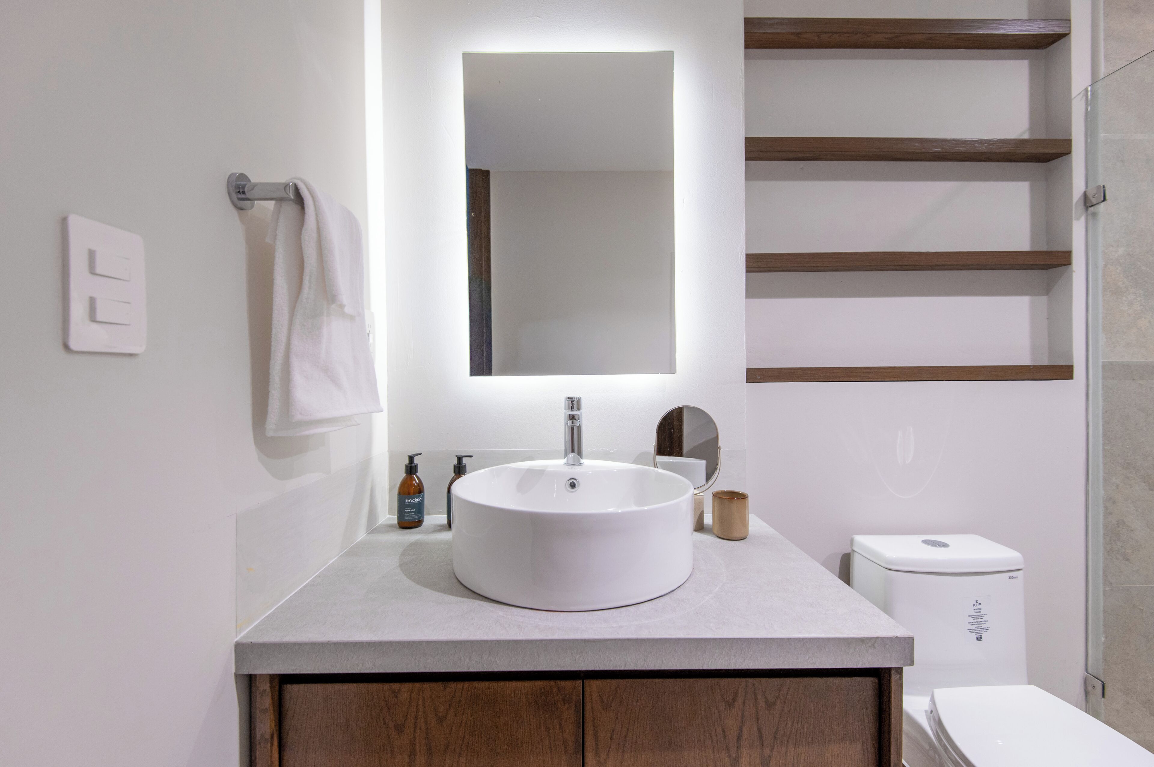 A modern bathroom with a round sink, a mirror, a towel rack, a toilet, and a shelf.