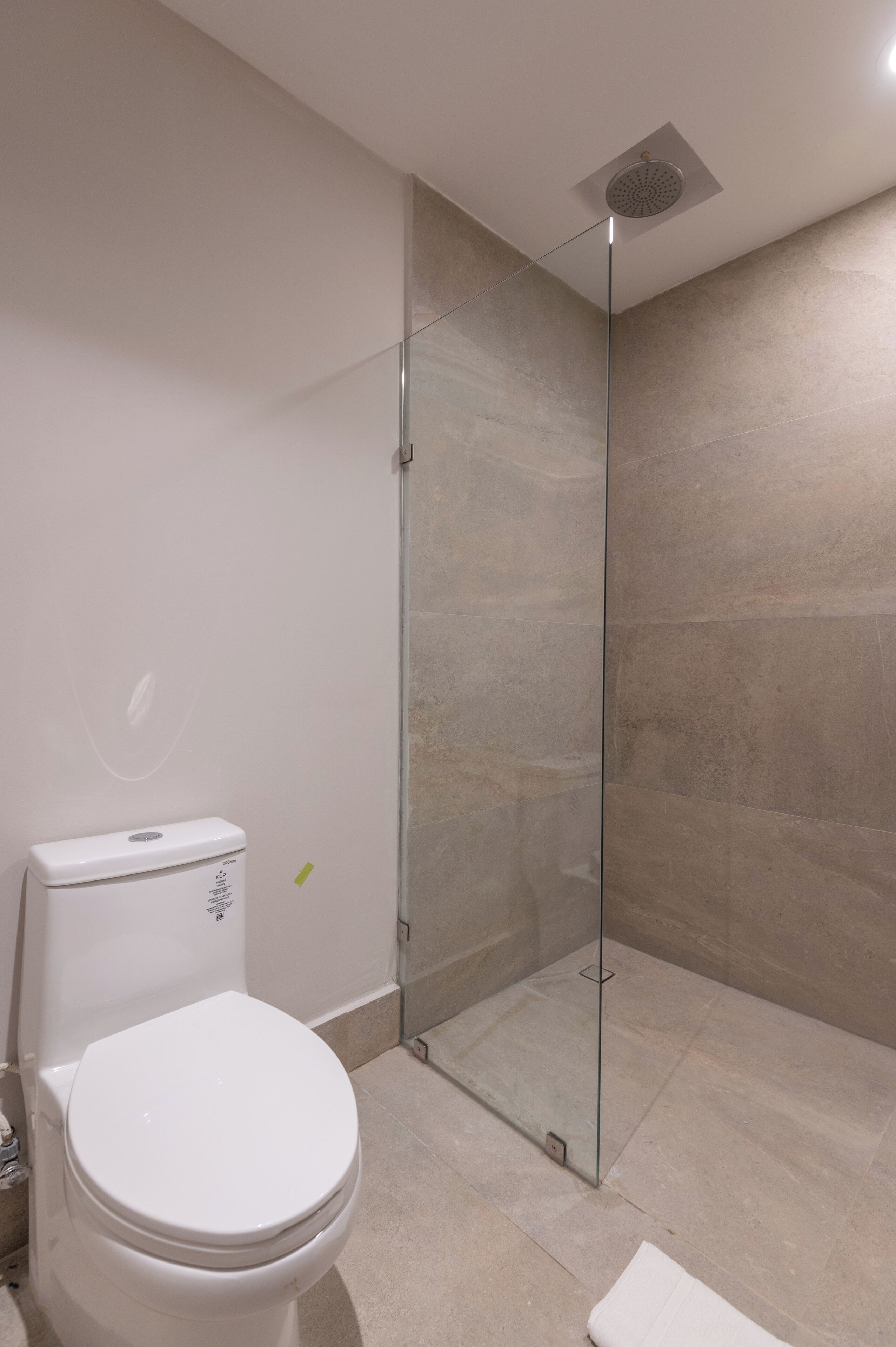 A modern bathroom with a toilet, a glass shower enclosure, and beige tiled walls.