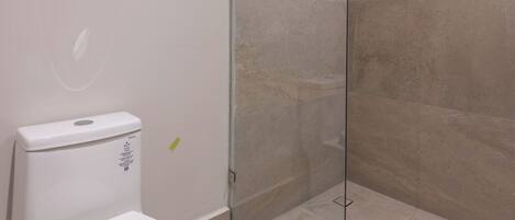 Un baño moderno con inodoro, cabina de ducha de vidrio y paredes con azulejos color beige.
