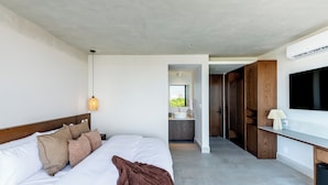 A modern hotel room with a large bed, a bedside lamp, a TV, and a bathroom with a sink and mirror.