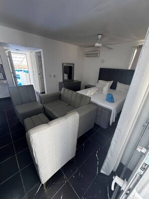 A hotel room with a sofa, a bed, a nightstand, a mirror, and a ceiling fan. - Condo Face à Épicerie à 3 Minutes de la Plage 302 (Sosúa)