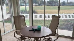 A room with a round table and two chairs, large windows with a view of a grassy area and a white fence, and a ceiling fan. - The Villages 2 bedroom / 2 bath home minutes from Lake Sumter Landing (The Villages)