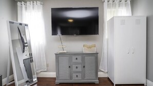 A room with a flat-screen TV mounted on the wall, a grey cabinet with drawers, and a white wardrobe.