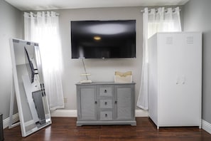 A room with a flat-screen TV mounted on the wall, a grey cabinet with drawers, and a white wardrobe.