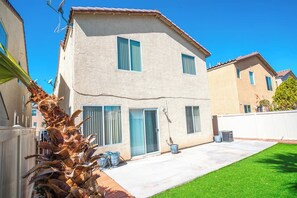 A two-story house with a flat roof, a front door, and a small front yard with a lawn and a palm tree. - 3BR Home Near Las Vegas Strip | Pet Friendly (Las Vegas)