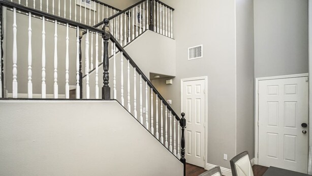 A staircase with white balusters and black handrails, leading to a landing with a white door and a dining area with chairs and a table.