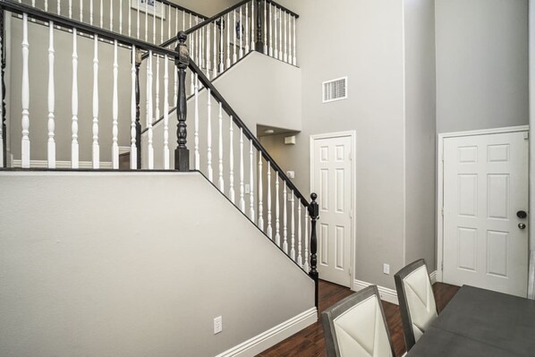 A staircase with white balusters and black handrails, leading to a landing with a white door and a dining area with chairs and a table.