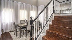 A dining area with a table and chairs, a staircase with wooden steps and white balusters, and a patterned rug on the floor.