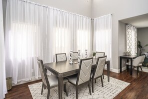 A dining area with a dark wooden table and chairs, white curtains, and a patterned rug. - 3BR Home Near Las Vegas Strip | Pet Friendly (Las Vegas)