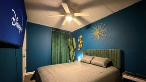 Quarto com cama, ventilador de teto, relógio de parede e um objeto decorativo na parede.