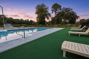 Ein Schwimmbecken mit einer Metallleiter, umgeben von grünem Kunstrasen und Holzliegen.