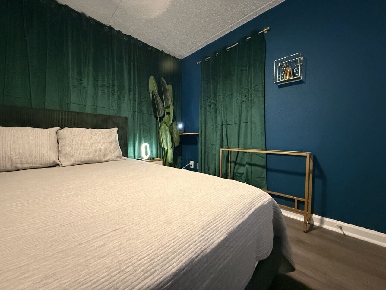 A bedroom with a bed, curtains, a bedside lamp, and a wall-mounted shelf.
