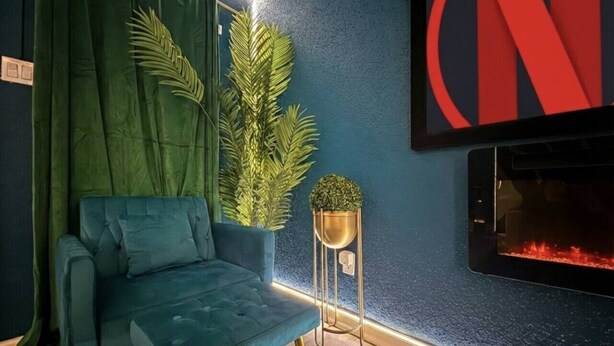 Uma sala de estar moderna com um sofá azul, cortinas verdes, uma pequena planta e uma lareira.