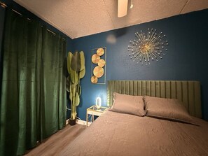 A bedroom with a bed, a nightstand, a wall art piece, and a curtain.