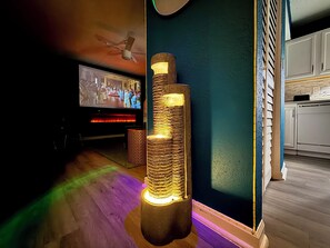Et værelse med fjernsyn, en høj, struktureret lampe og et tekøkken.