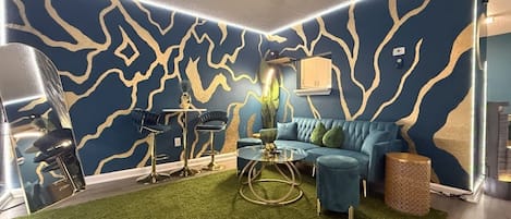 A room with a blue and gold patterned wall, a blue sofa, a round coffee table, and a green carpet.