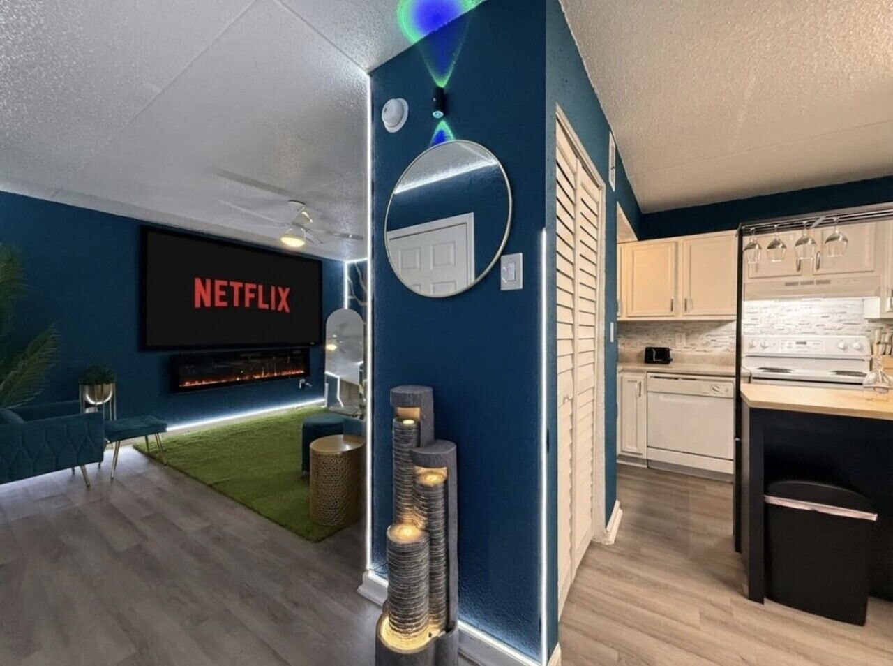 A modern living room with a Netflix screen, a fireplace, and a kitchen area with white cabinets.