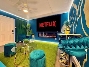 Ett modernt vardagsrum med en platt-TV som visar "NETFLIX", en takfläkt, en soffa, ett soffbord och en liten växt.