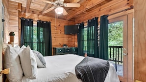 Een slaapkamer in een houten chalet, met een bed, gordijnen, een televisie en een balkon.