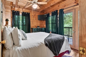 Ein Schlafzimmer einer Holzhütte mit Bett, Vorhängen, einem Fernseher und einem Balkon.