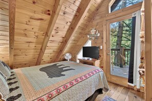 A cozy cabin bedroom with a bed, a TV, and a sliding door to a deck. - Hot Tub, Sauna, Pool Table, Free Dollywood, Spa (Gatlinburg)