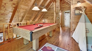 Een houten interieur met een pooltafel, houten balken in het plafond en een tipi-achtige constructie.