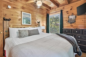 A wooden cabin bedroom with a bed, pillows, a nightstand, a dresser, and a ceiling fan. - Hot Tub, Sauna, Pool Table, Free Dollywood, Spa (Gatlinburg)