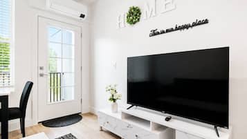 Een moderne woonkamer met een grote flatscreen-tv, een witte tv-kast, een deur met raam en een bordje met de tekst 'HOME' erboven.