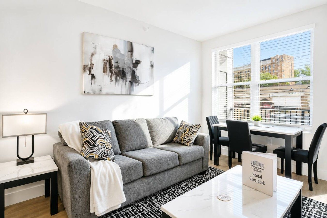 Een moderne woonkamer met een grijze bank, gestreepte kussens, een witte salontafel en een schilderij aan de muur.