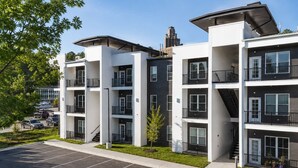 A multi-story residential building with balconies, a parking lot, and a clear sky. - Charming 1 BR • Balcony • Free Parking • Downtown (Hot Springs)