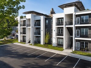 Un edificio residencial de varios pisos con balcones, un estacionamiento y cielo despejado.