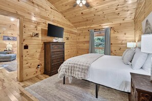 Ein Schlafzimmer einer Holzhütte mit einem Bett, einer Kommode und einem an der Wand befestigten Fernseher.