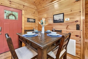 A wooden interior with a dining table set for four, surrounded by chairs with cushions. - Free Tickets,Sauna,Cold Plunge,Gatlinburg, 1 level (Gatlinburg)