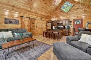 Ein gemütliches Blockhaus-Interieur mit Holzausstattung, einer Couch, einem Couchtisch, einer Küchenzeile und einem Essbereich.
