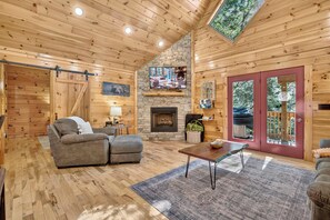 L’intérieur d’un chalet accueillant, avec une cheminée en pierre, des murs en bois et une grande fenêtre.