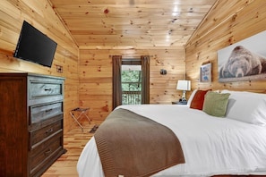 A wooden-paneled room with a bed, a television, a dresser, and a window with curtains. - Free Tickets,Sauna,Cold Plunge,Gatlinburg, 1 level (Gatlinburg)