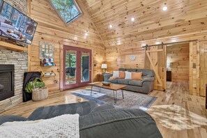 A cozy cabin interior with a fireplace, a sofa, a coffee table, and a large window. - Free Tickets,Sauna,Cold Plunge,Gatlinburg, 1 level (Gatlinburg)